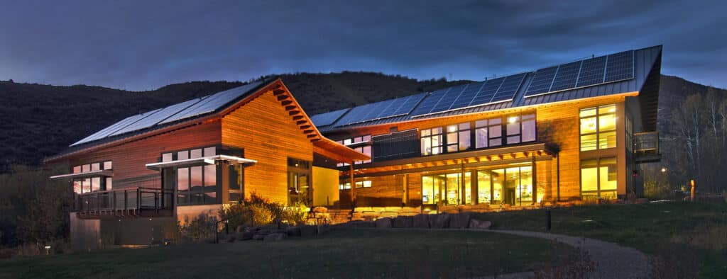 Walking Mountains Science Center in Avon, Colorado, at dusk, with rooftop solar panels and lit timber-framed buildings